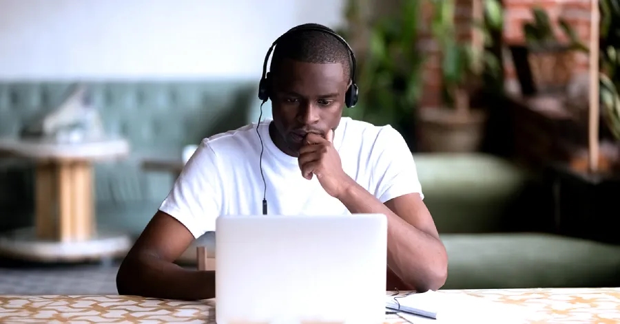 A focused African American man wearing headphones, immersed in cloud-based E-Learning on his laptop.
