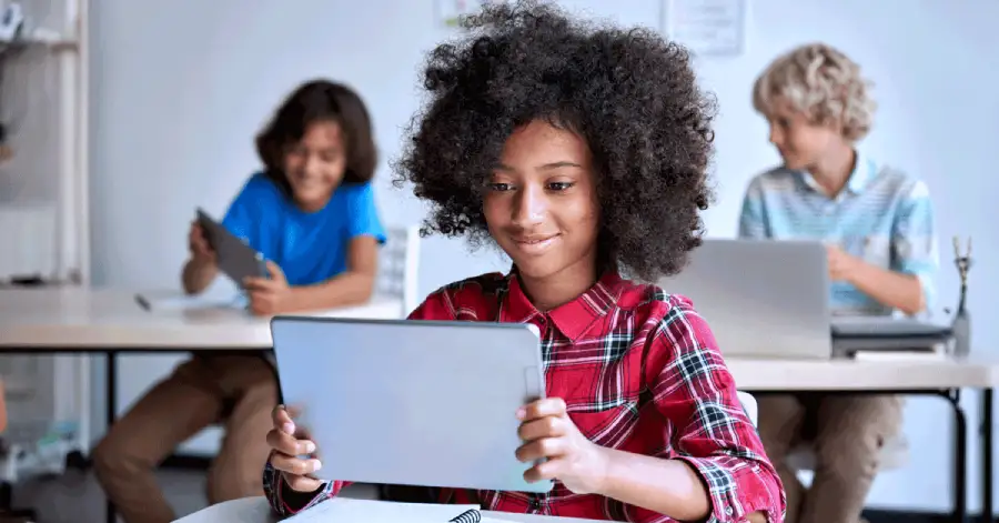A happy teen school girl sits engrossed on her digital tablet, exploring the world of AI in K-12 education.