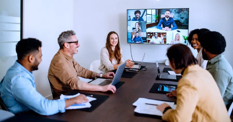 A lively and productive blended training team meeting is captured where colleagues are connected via a large screen, showcasing a blend of in-person and remote collaboration.