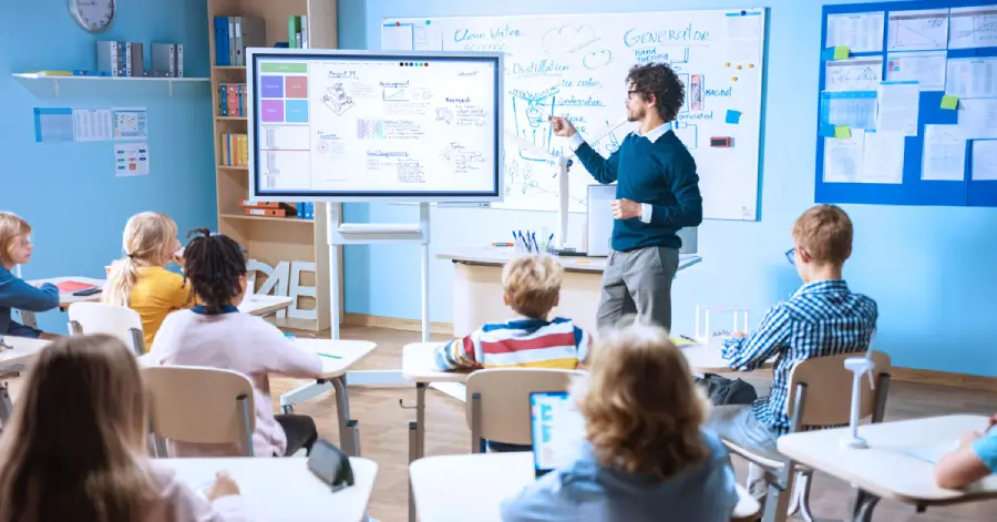  A teacher standing in front of a digital whiteboard in a classroom discussing AI tools in education.