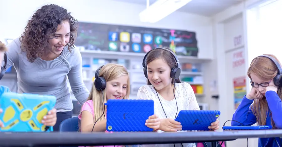 A group of three children learning through their tablets and a teacher guiding them.