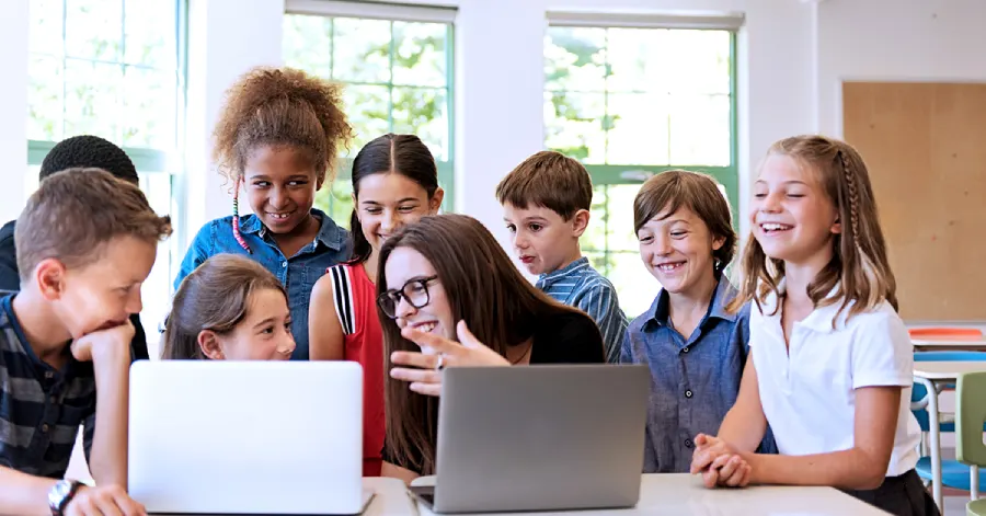 A multi-racial group of students with two laptops and a teacher teaching them about content migration.